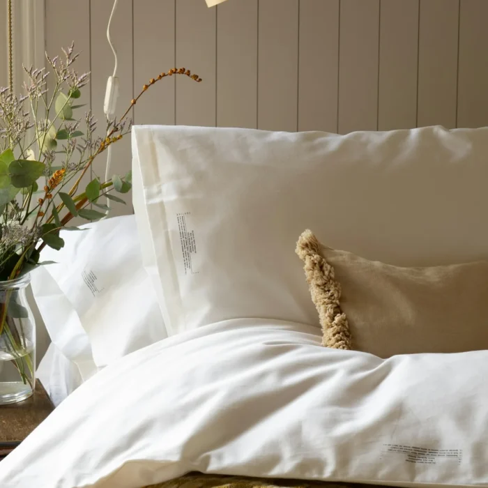 Ivory sateen pillow shams layered on a soft duvet in a sunlit bedroom