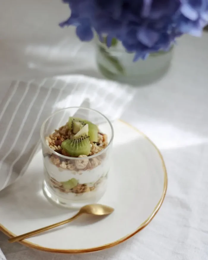 Gold-rimmed white dessert plate with a fruit parfait glass and gold spoon in bright natural light