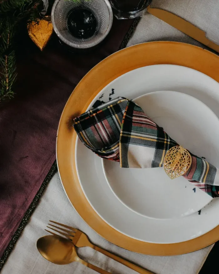 White dinner plates layered on a gold charger plate with a tartan napkin, elegant table setting