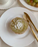 White porcelain dinner plate with a fruit tart and gold cutlery on a cream tablecloth