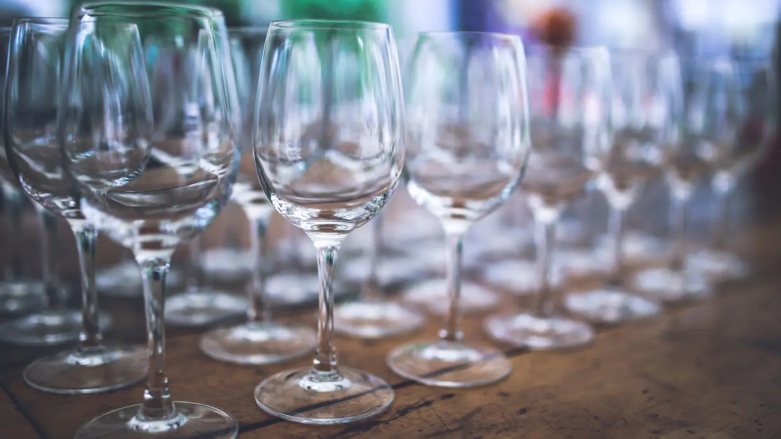 Rows of empty crystal wine glasses on a rustic wooden table, set out for a dinner party
