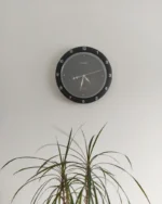 Halo minimal wall clock with a dark dial above a leafy dracaena plant in a calm white room