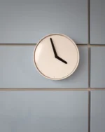 Halo minimal wall clock with a cream dial and bold black hands on a soft grey tiled wall