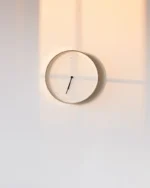Halo minimal wall clock on a white wall, catching warm evening light and soft shadows