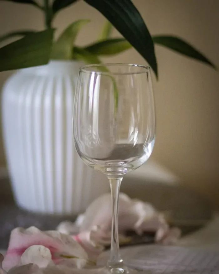 Empty Lumière crystal wine glass styled with pink petals and a white ribbed vase on a side table