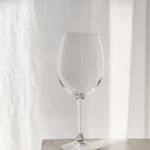 Empty Lumière lead-free crystal wine glass on a sunlit wooden table against a soft white curtain
