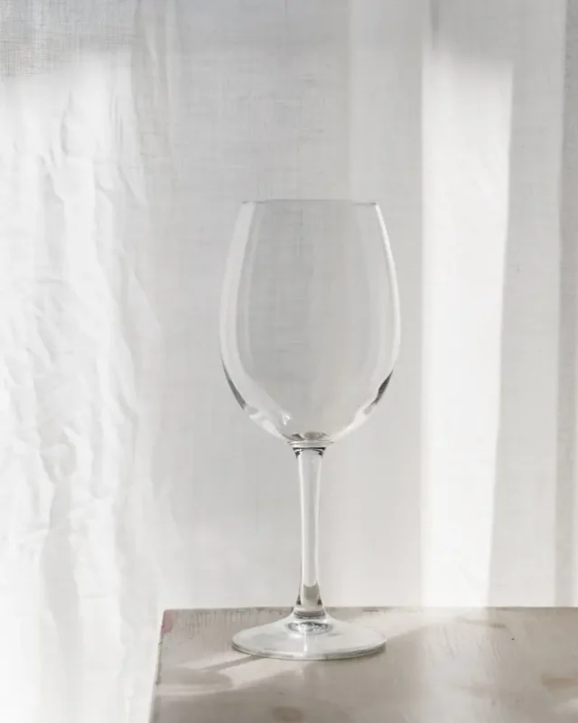 Empty Lumière lead-free crystal wine glass on a sunlit wooden table against a soft white curtain