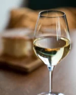 Lumière crystal wine glass of white wine on a wooden dinner table with bread softly blurred behind