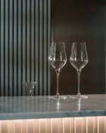 Two empty Lumière crystal wine glasses on a marble bar counter in a modern, softly lit interior