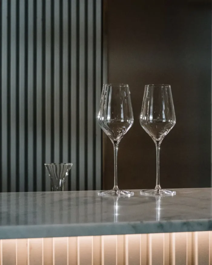 Two empty Lumière crystal wine glasses on a marble bar counter in a modern, softly lit interior