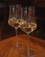 Pair of Lumière crystal wine glasses with white wine on a warm wooden table in a cosy room