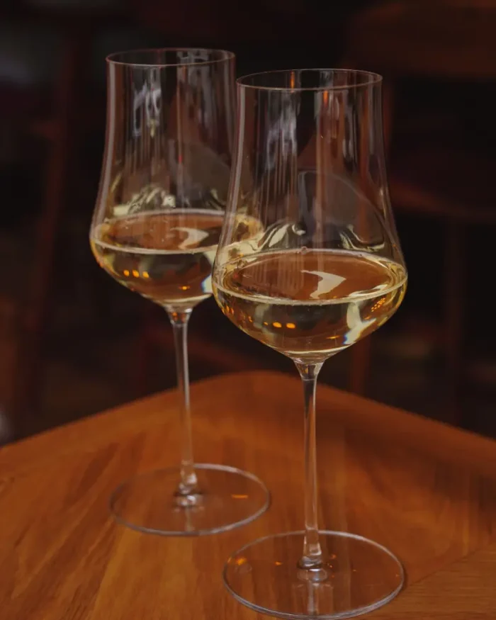 Pair of Lumière crystal wine glasses with white wine on a warm wooden table in a cosy room